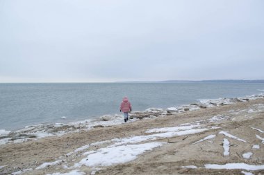 Genç kadın kış sahilde yürüyor.