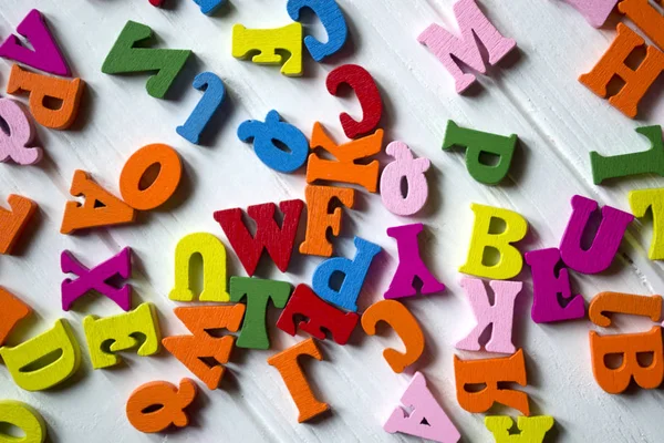 Multicolor letters on a white wooden background. Colorful wooden alphabet on a table.