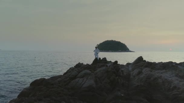 Hombre de blanco en la playa del atardecer en Tailandia rocas — Vídeo de stock