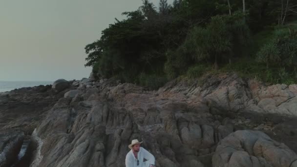 Man in wit op sunset beach in Thailand rotsen — Stockvideo