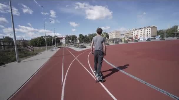 Elektrische Longboard zomer rit op rode sport stadion met speeltuin — Stockvideo