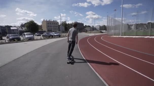 Longboard eléctrico paseo de verano en el estadio deportivo rojo con parque infantil — Vídeo de stock