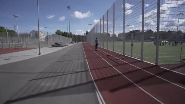 Longboard eléctrico paseo de verano en el estadio deportivo rojo con parque infantil — Vídeo de stock