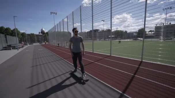 Longboard eléctrico paseo de verano en el estadio deportivo rojo con parque infantil — Vídeo de stock