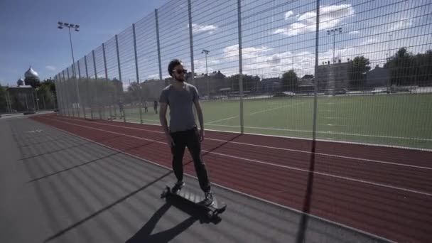 Elektrische Longboard zomer rit op rode sport stadion met speeltuin — Stockvideo