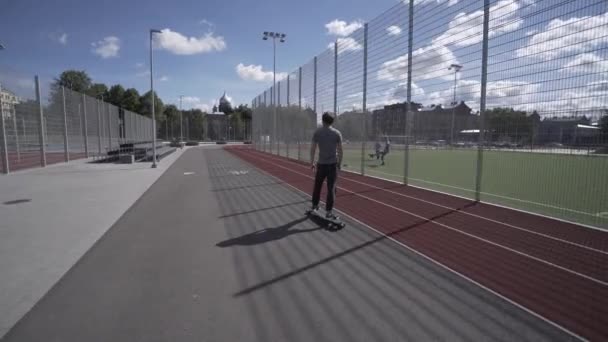 Longboard électrique balade d'été sur le stade de sport rouge avec aire de jeux — Video