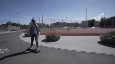 Elektrik Longboard adam yeşil gömlek ve şapka kırmızı spor Stadyumu Bahçesi ile binmek