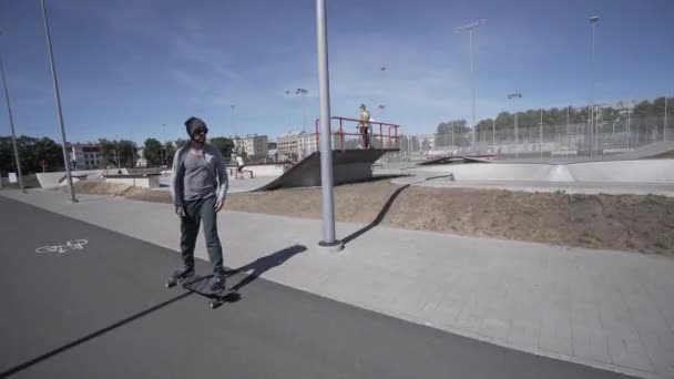 Longboard électrique homme en chemise verte et chapeau tour sur le stade de sport rouge avec aire de jeux — Video