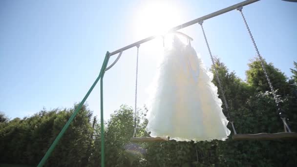 Robe de mariée blanche suspendue à une balançoire verte dans le jardin — Video