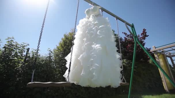 White Wedding dress hanging on a green swing in the garden — Stock Video