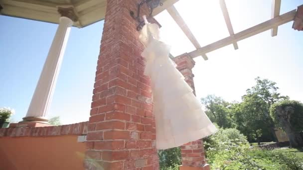 Vestido de novia blanco colgado junto a una pared de ladrillo rojo en un día soleado perezoso antes de la ceremonia — Vídeos de Stock