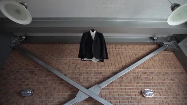 A mans jacket and suit hangs on a hanger near a red brick wall before the grooms wedding — Stock Video