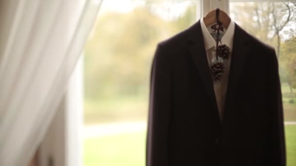 Мужская куртка и костюм висят на вешалке перед свадьбой женихов, висящей у окна — стоковое видео