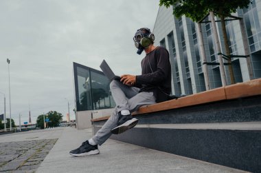 Bir laptop telefon ve kulaklıklar ile şehirde bir gaz maskesi bir adam