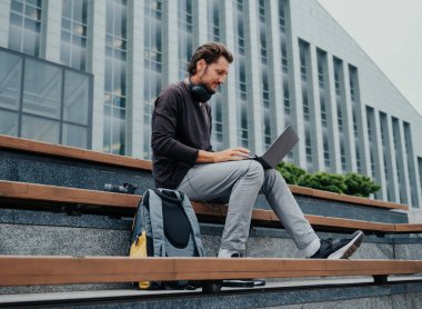 Büyük kentsel şehirde Freelancer Man bir laptop telefon kamera ile çalışan ve kulaklıklar üzerinden müzik dinleme