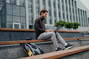 Büyük kentsel şehirde Freelancer Man bir laptop telefon kamera ile çalışan ve kulaklıklar üzerinden müzik dinleme