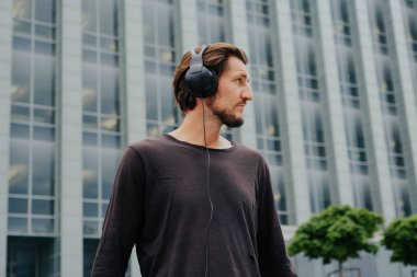 Büyük kentsel şehirde Freelancer Man bir laptop telefon kamera ile çalışan ve kulaklıklar üzerinden müzik dinleme