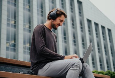 Büyük kentsel şehirde Freelancer Man bir laptop telefon kamera ile çalışan ve kulaklıklar üzerinden müzik dinleme