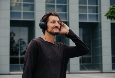 Büyük kentsel şehirde Freelancer Man bir laptop telefon kamera ile çalışan ve kulaklıklar üzerinden müzik dinleme