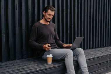 Freelance adam bir laptop telefon kamera ve misik kulaklıklar ile kahve veya çay ile kentsel şehirde siting