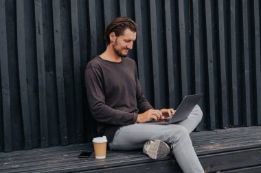 Freelance adam bir laptop telefon kamera ve misik kulaklıklar ile kahve veya çay ile kentsel şehirde siting