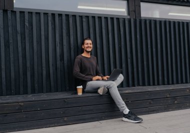 Freelance adam bir laptop telefon kamera ve misik kulaklıklar ile kahve veya çay ile kentsel şehirde siting