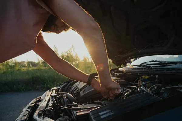 Mladý muž opravuje auto při západu slunce mimo město — Stock fotografie