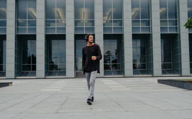 Bir laptop telefon kamera ile çalışan büyük kentsel şehirde Freelancer Man yürüyüş ve kulaklıklar üzerinden müzik dinleme