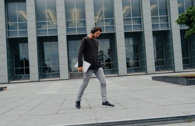 Bir laptop telefon kamera ile çalışan büyük kentsel şehirde Freelancer Man yürüyüş ve kulaklıklar üzerinden müzik dinleme