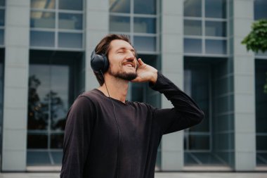 Büyük kentsel şehirde Freelancer Man bir laptop telefon kamera ile çalışan ve kulaklıklar üzerinden müzik dinleme