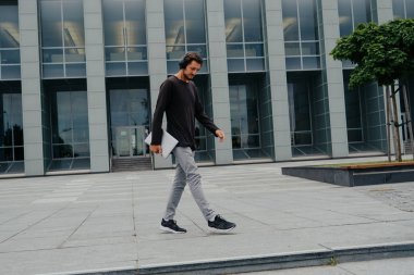 Bir laptop telefon kamera ile çalışan büyük kentsel şehirde Freelancer Man yürüyüş ve kulaklıklar üzerinden müzik dinleme