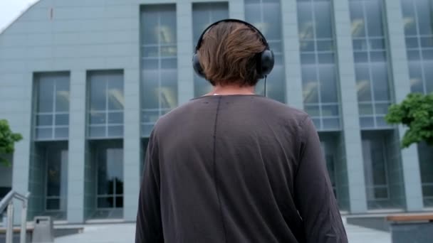 Freelancer Man walking in the big urban city working with a laptop phone camera and listening music via headphones — Stock Video