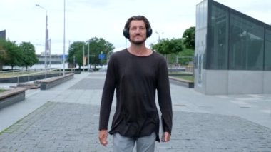 Freelancer Man büyük şehir şehirde bir dizüstü telefon kamerası ile çalışan yürüyüş ve kulaklık ile müzik dinleme