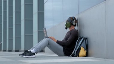 Bir laptop telefon ve kulaklıklar ile şehirde bir gaz maskesi bir adam