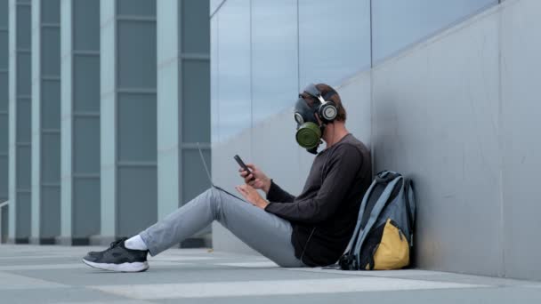 Bir laptop telefon ve kulaklıklar ile şehirde bir gaz maskesi bir adam — Stok video