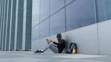 Bir laptop telefon ve kulaklıklar ile şehirde bir gaz maskesi bir adam