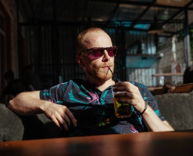 Güneş gözlüklü adam limonata içer ve öğle yemeğini bekler.