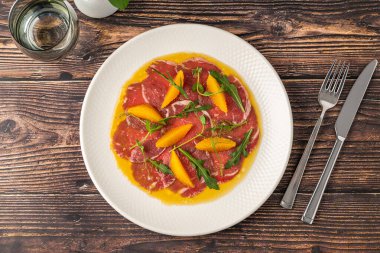 İnce dilimlenmiş et carpaccio portakal dilimleri ve roka yapraklarıyla.
