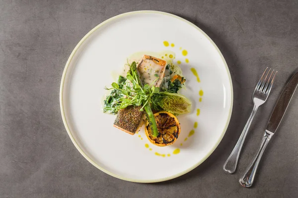 Izgara somon fileto, kömürleşmiş limon ve tabakta yeşillikler.