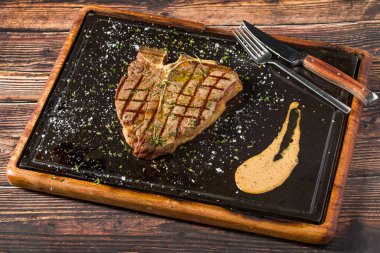 Klasik T-Bone bifteği ızgara ve sıcak taş tahtada servis ediliyor.