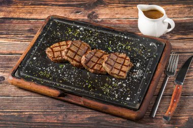 Izgara sığır filetosu, siyah taş tabakta otlarla servis edilir.