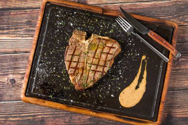 Klasik T-Bone bifteği ızgara ve sıcak taş tahtada servis ediliyor.