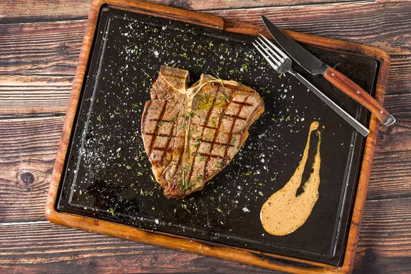 Klasik T-Bone bifteği ızgara ve sıcak taş tahtada servis ediliyor.