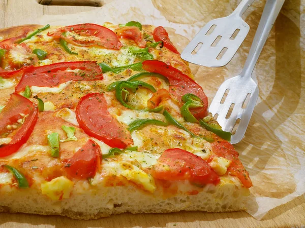 Pizza with tomato and green pepper. Fresh baked piece of pizza and tongs.