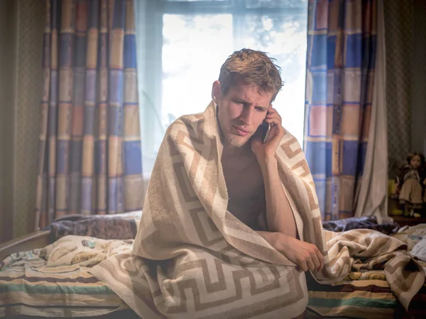Молодой Человек Сидит Кровати Одеялом Телефоном Трауре — стоковое фото