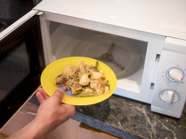 yakın yukarı el mikrodalga fırında kızarmış sebzeler ile plaka koyar