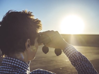 Adam arkadan görünüm kadar güneşin karşı günbatımı sırasında seyir dürbün ile yakın