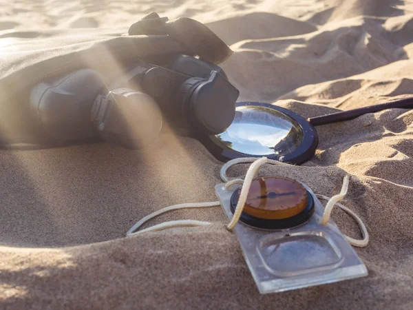 close up compass magnifier and binoculars on the sea sandy coast on a summer sunny day