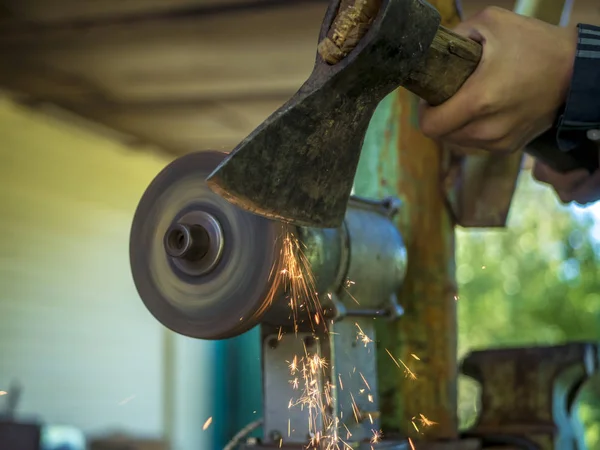 using electric grinder, hands holding axe close up