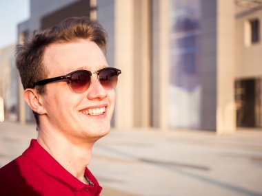 Kırmızı gömlek ve güneş gözlüğü takan yakışıklı genç portre gülüyor